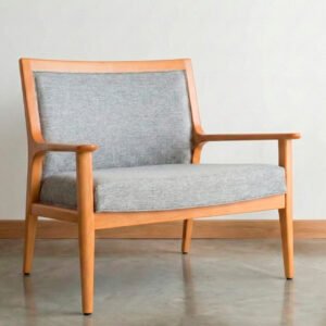 Butacón de estilo nórdico con estructura de madera clara, apoyabrazos integrados y tapizado en tela gris melange, ubicado en un ambiente minimalista con piso de cemento y pared blanca.