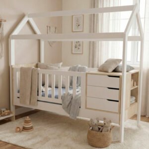 Cuna funcional de madera con estructura en forma de casita, color blanco y madera natural, que incluye baranda de seguridad, cajonera lateral de tres niveles y estantería abierta en el piecero sobre fondo blanco.