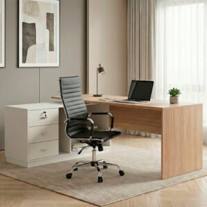 Vista de un escritorio de oficina moderno con forma de L. La superficie principal es de melamina color madera clara apoyada sobre un lateral sólido y, en el otro extremo, sobre un módulo bajo de color ceniza que contiene tres cajones con llave y estantes abiertos. El conjunto está ubicado en una oficina iluminada con suelo de cemento alisado