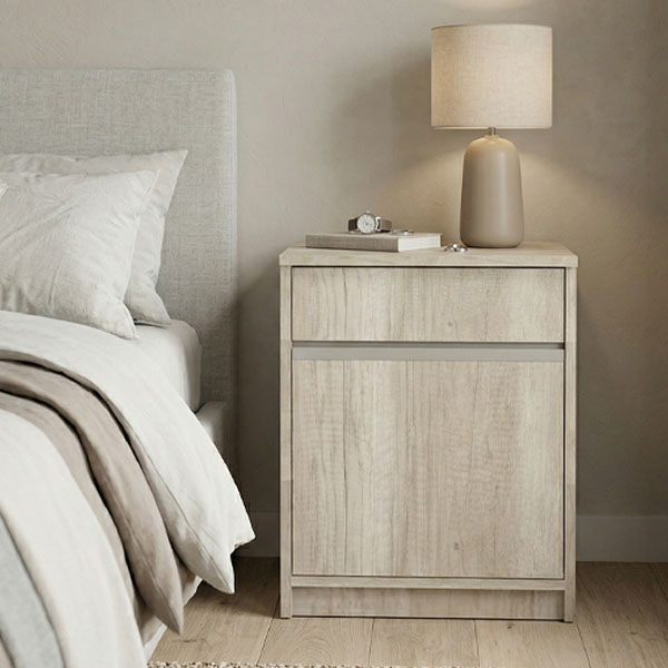 Mesa de luz moderna modelo Stylus fabricada en melamina color Helsinki, con diseño de líneas puras, un cajón superior y una puerta, ambientada en un dormitorio de tonos neutros.