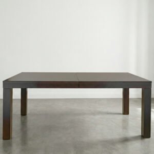 Mesa de comedor rectangular modelo Mónaco, extensible y de color marrón oscuro, con patas gruesas y diseño minimalista sobre suelo de cemento