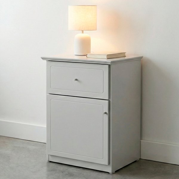 Mesa de luz de madera color blanco con un cajón superior y un compartimento inferior de puerta, detalles de molduras rectangulares y tiradores metálicos mínimos sobre un fondo neutro de estudio.