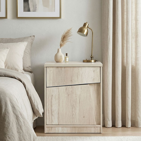Mesa de luz modelo Kendor fabricada en melamina Helsinki de color madera clara, con un diseño de frente geométrico y líneas oblicuas, ubicada en un dormitorio de estilo nórdico y tonos neutros.