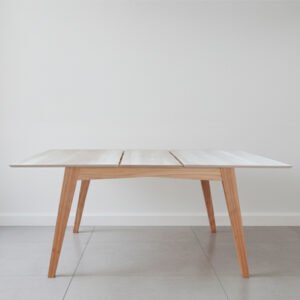 Mesa de comedor extensible modelo Andrea con patas de madera maciza de paraíso y tapa de MDF enchapada en melamina color Helsinki sobre un fondo blanco minimalista.