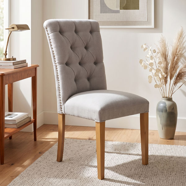 Silla de comedor tapizada Silla Gracia en tela beige con tufting de capitoné y tachuelas metálicas, sobre fondo blanco aislado.