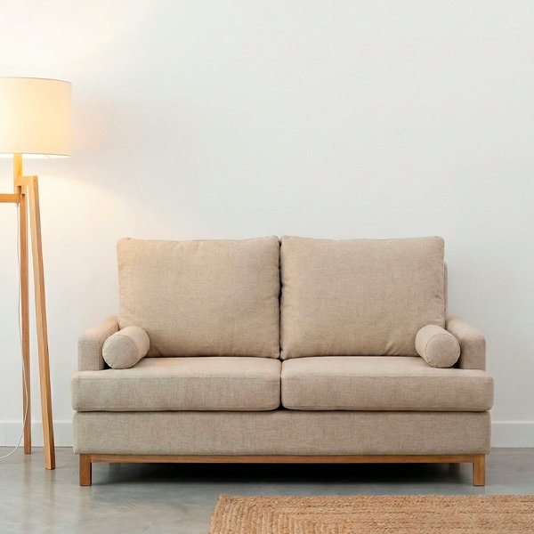 Sofá modelo Bambú de dos cuerpos tapizado en tela color natural, ubicado en una sala moderna con piso de cemento alisado, lámpara de pie y estantería de madera.