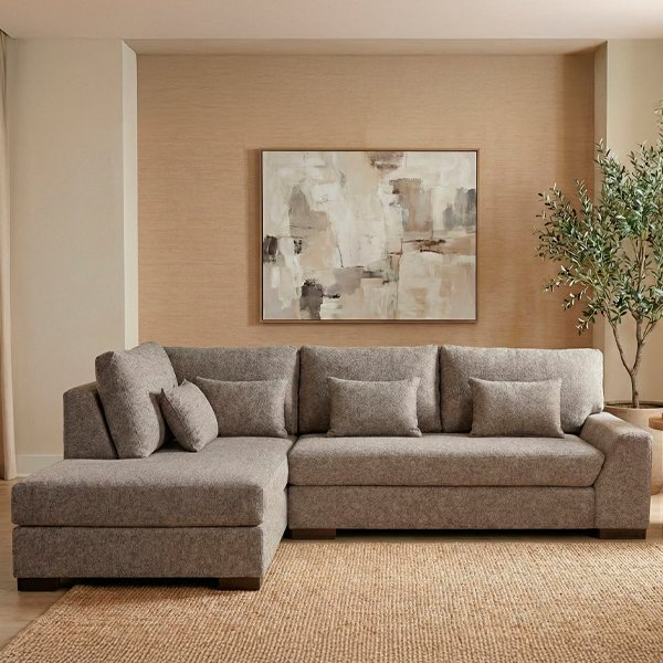 Sofá esquinero Liverpool tapizado en tela color gris topo con diseño en L, cojines de respaldo mullidos y patas de madera, sobre fondo blanco minimalista.