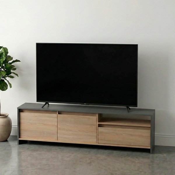 Mueble rack para TV de madera clara con estructura gris oscuro, ubicado en una sala con piso de microcemento, pared blanca y decoración con planta y lámpara de pie cálida.