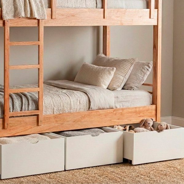 Tres cajones de melamina blanca de diferentes tamaños alineados horizontalmente, con tiradores uñeros semicirculares y ruedas ocultas en la base, sobre un fondo gris neutro.