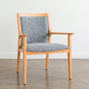 Sillón Olsen Classic de madera clara con respaldo y asiento tapizados en tela gris texturizada sobre un piso de cemento alisado.