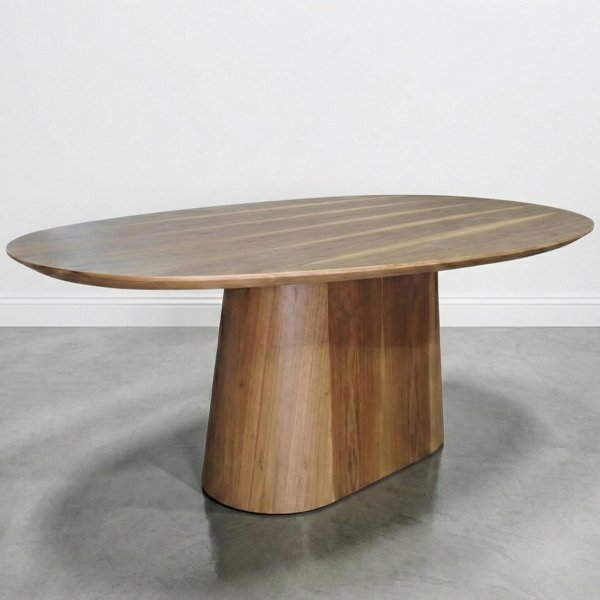 Mesa de comedor de madera de petiribí con tapa de forma orgánica ovalada y base central de pedestal sólida, sobre un piso de cemento alisado y fondo blanco.