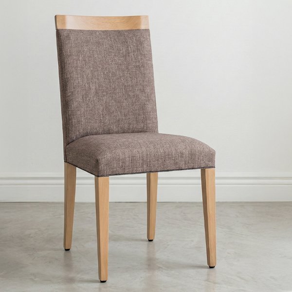 Silla de comedor modelo Dente fabricada en madera maciza de guatambú con asiento y respaldo tapizados en tela color visón, ambientada en un espacio moderno con luz natural.