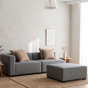 Sofá modular Gabo de tela gris compuesto por módulo con brazo, módulo sin brazo y puff en un living minimalista iluminado con luz natural.